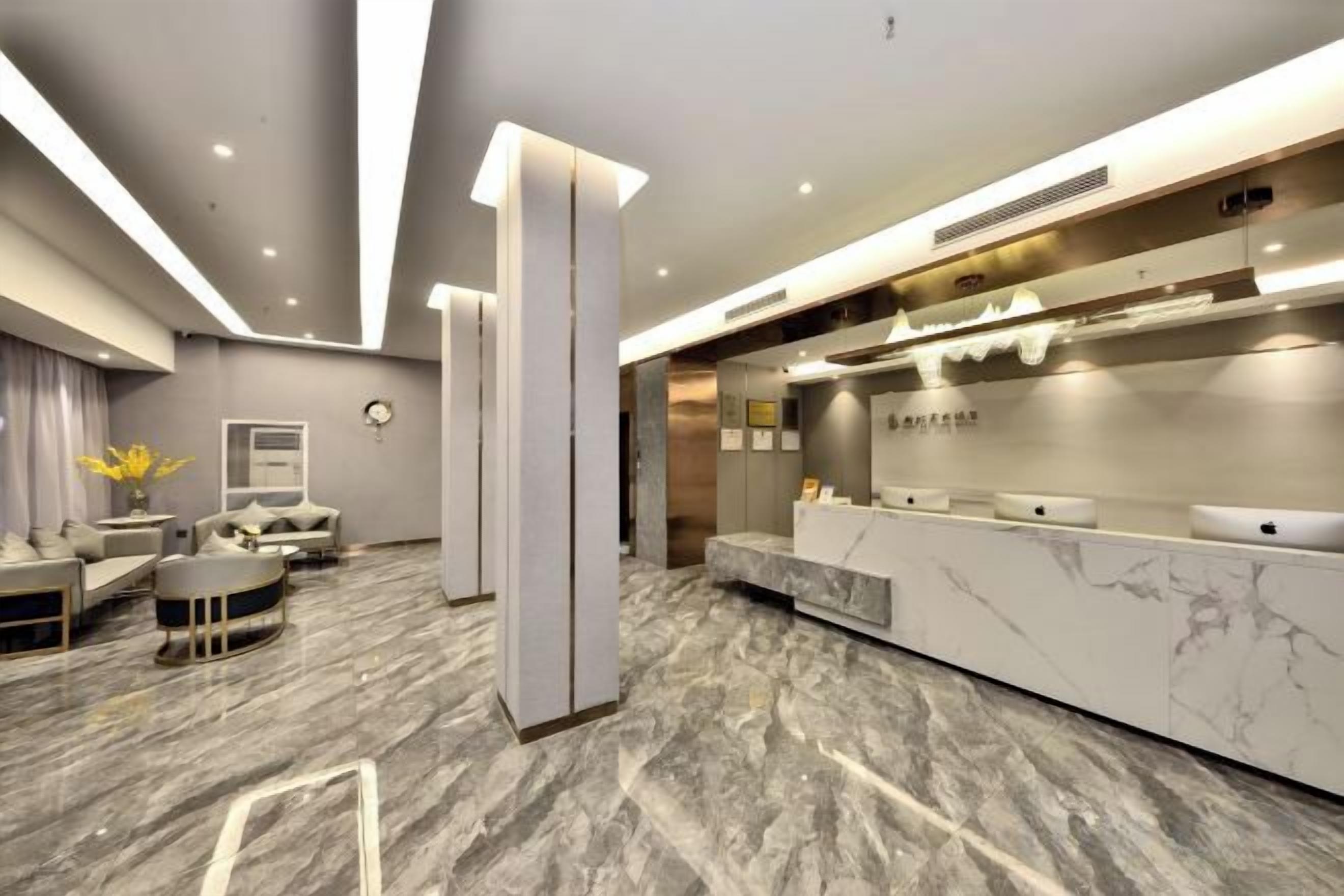 A modern hotel lobby with a reception desk, seating area, and a marble floor.