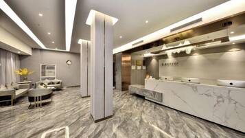 A modern hotel lobby with a reception desk, seating area, and a marble floor.