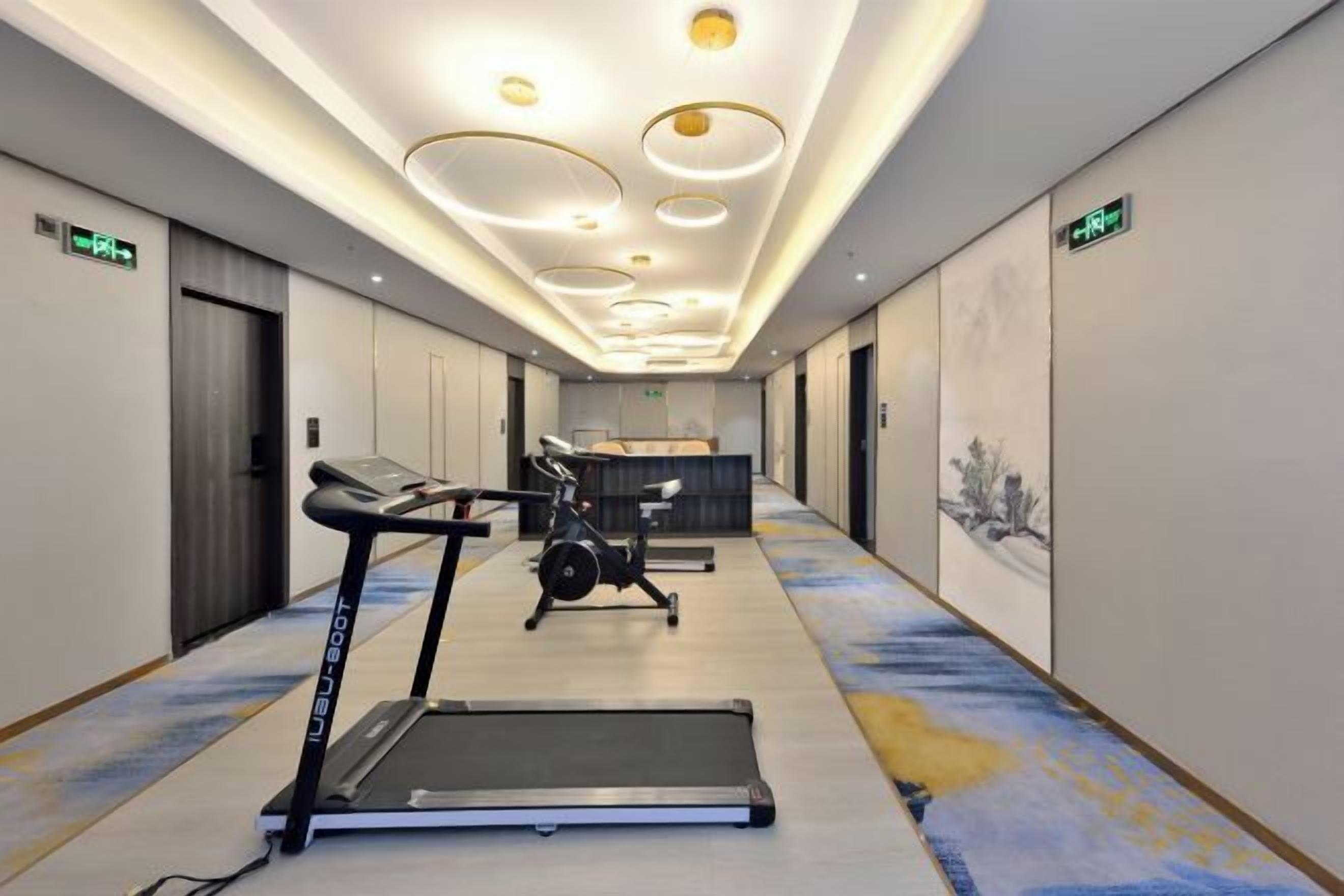 A hotel corridor with exercise equipment, including treadmills and a stationary bike, and a reception desk.