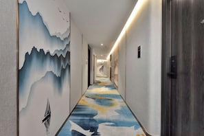 Un pasillo con un mural de montañas y un velero, alfombra estampada y un ascensor moderno.
