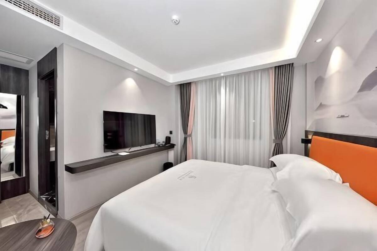 A modern hotel room with a bed, a TV, a desk, and a bathroom.