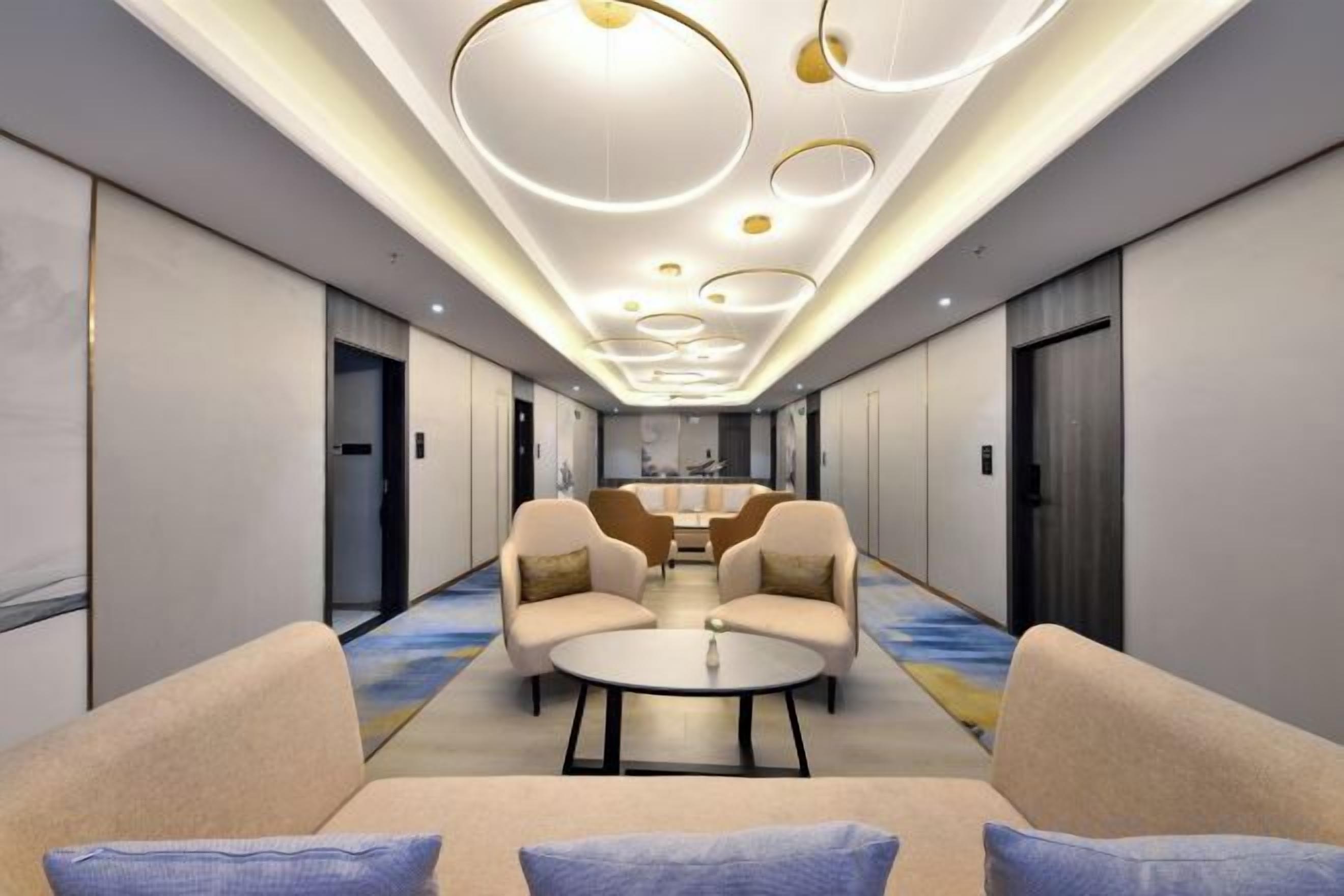 A hotel lobby with a central seating area, a reception desk, and a corridor leading to elevators.