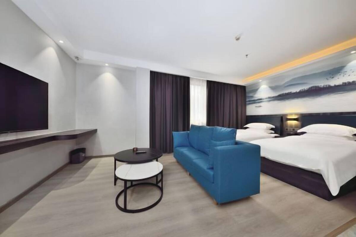 A modern hotel room with a sofa, a bed, a small round table, and a TV mounted on the wall.