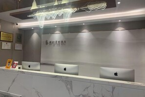 Un comptoir d’accueil avec trois ordinateurs portables Apple, un plan de travail en marbre et un mur orné d’un logo.