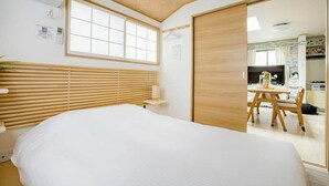 Un dormitorio con cama, persianas de madera, una ventana y un acceso corredizo a una zona de cocina.