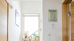 Una escalera de madera que conduce a una habitación con ventana, un cartel en la pared con normas de la casa y un pequeño estante con objetos.