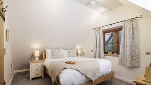 Ein Schlafzimmer mit einem hölzernen Bett, zwei Nachttischen mit Lampen, einem Fenster mit Vorhängen und Blick auf Bäume.