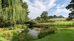 Ein friedlicher Garten mit Teich, üppigem Grün und einem Gebäude in der Ferne.