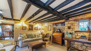 A cozy room with a stone wall, wooden beams, a sofa, a wooden chest of drawers, and a window with a view. - Characterful holiday cottage in the heart of Bourton-on-the-Water - Pear Tree Cottage, Bourton (Cheltenham)