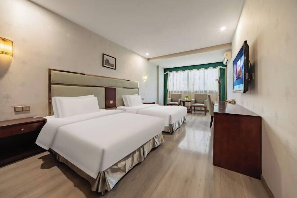 Une chambre d’hôtel avec deux lits, un bureau, une chaise et un téléviseur fixé au mur.