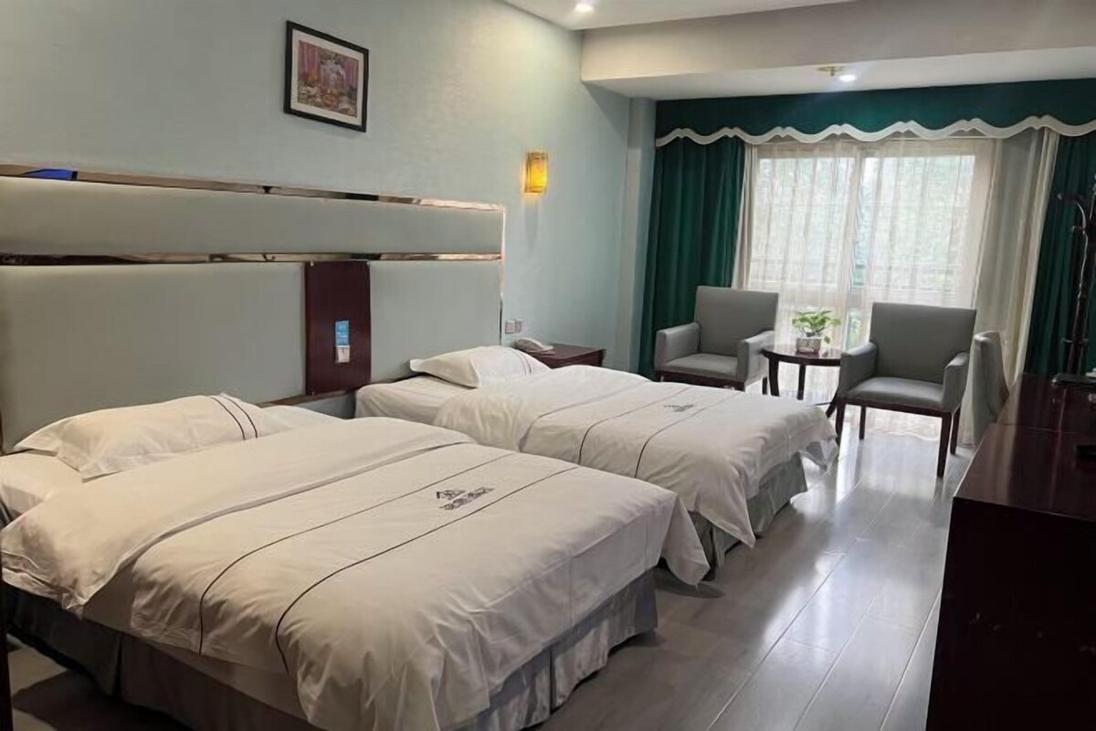 A hotel room with two beds, a desk, a chair, and a window with curtains.