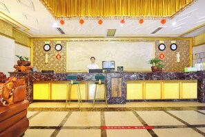 Un espace d’accueil d’hôtel avec un comptoir en marbre, un réceptionniste et une horloge au mur.