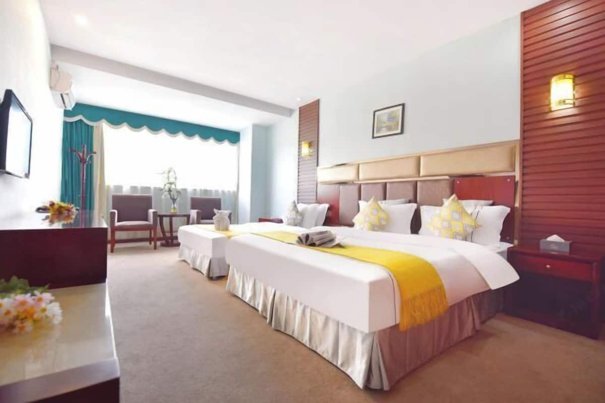 A hotel room with a large bed, a desk, and a chair. There is a window with a view of the outside.