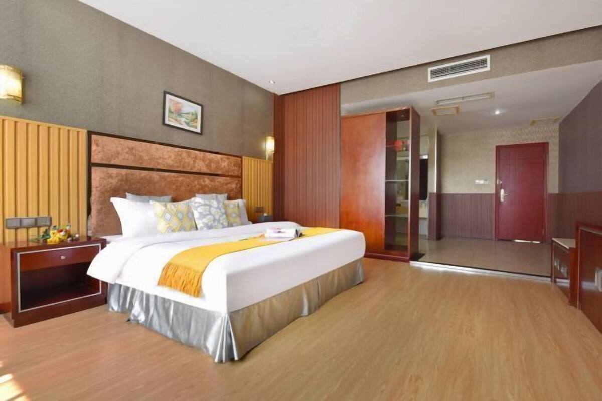 Une chambre d’hôtel avec un grand lit, une tête de lit en bois, une table de chevet et une armoire.
