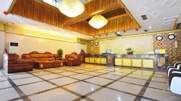 A hotel lobby with a check-in counter, seating area, and a chandelier.