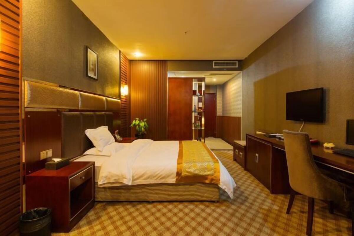 Une chambre d’hôtel équipée d’un lit, d’un bureau, d’une chaise, d’une télévision et d’une poubelle.