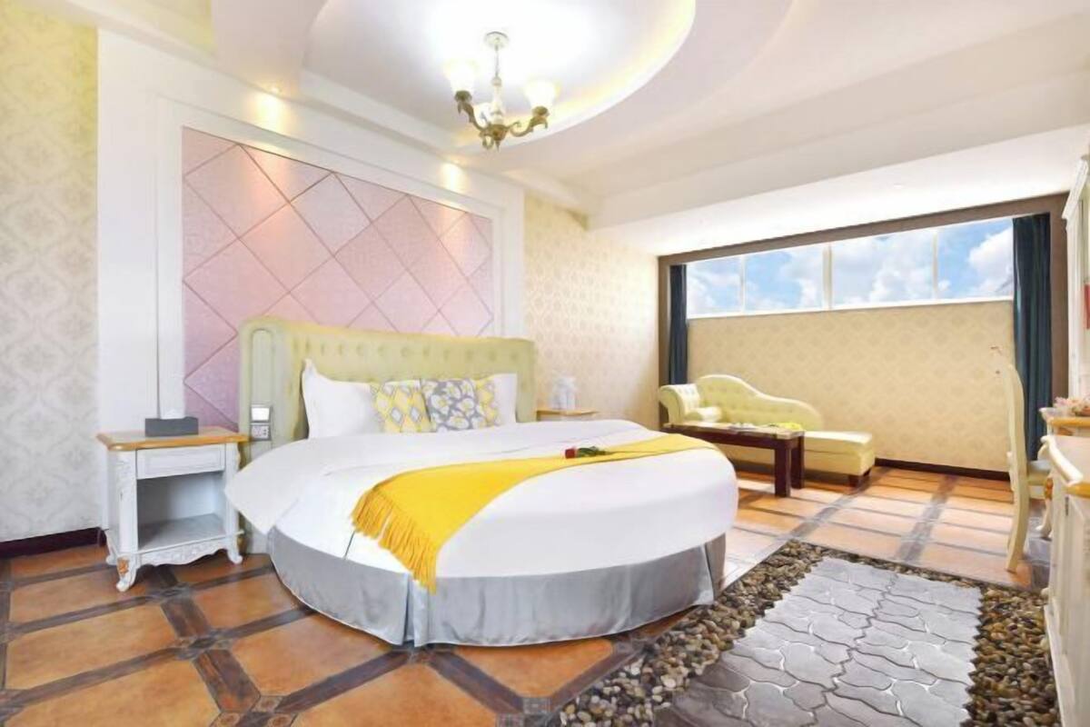 Une chambre d’hôtel avec un grand lit, une table de chevet, une chaise et une vue sur le ciel par une grande fenêtre.
