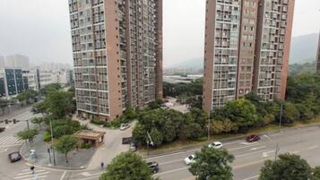 A high-rise residential building with multiple floors, surrounded by greenery and a road with vehicles.