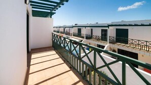 A balcony with a green railing overlooking a row of white buildings with balconies. - La Pituca Apartment (Playa Blanca)