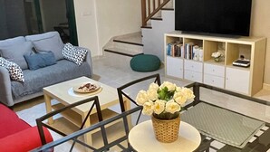 A modern living room with a glass coffee table, a sofa, a TV, and a staircase. - La Pituca Apartment (Playa Blanca)