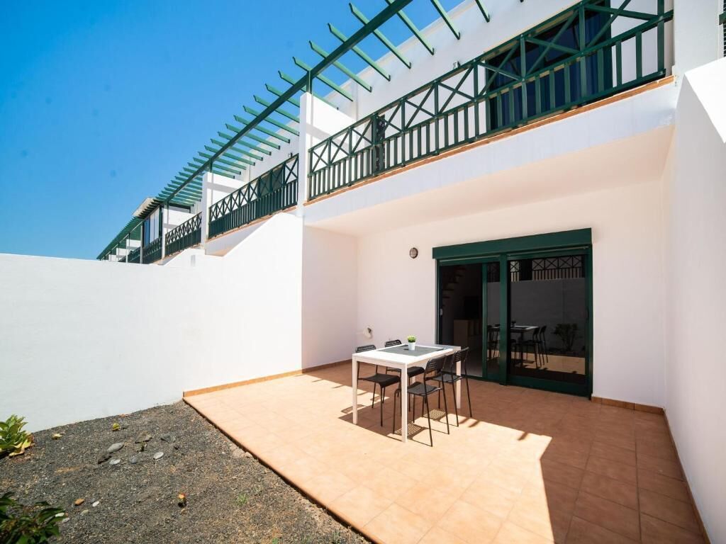 Eine Terrasse mit Tisch und Stühlen, eine Tür und ein Balkon mit Geländer.