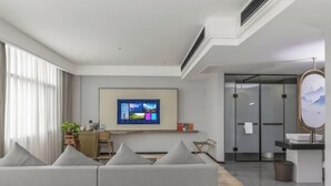 A modern hotel room with a sofa, a flat-screen TV, a desk, a bathroom with a mirror, and a view of the outdoors. - JAUNTYO INTERNATIONAL HOTEL (Dayu)