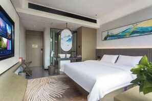 Ein modernes Hotelzimmer mit einem großen Bett, einem Fernseher, einem Spiegel und einem Bild an der Wand.