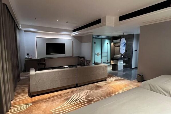 Una habitación de hotel moderna con sofá, televisión de pantalla plana, zona de comedor y baño con espejo.