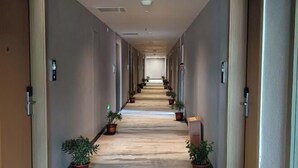 A hotel hallway with a carpeted floor, potted plants, and doors on either side. - JAUNTYO INTERNATIONAL HOTEL (Dayu)