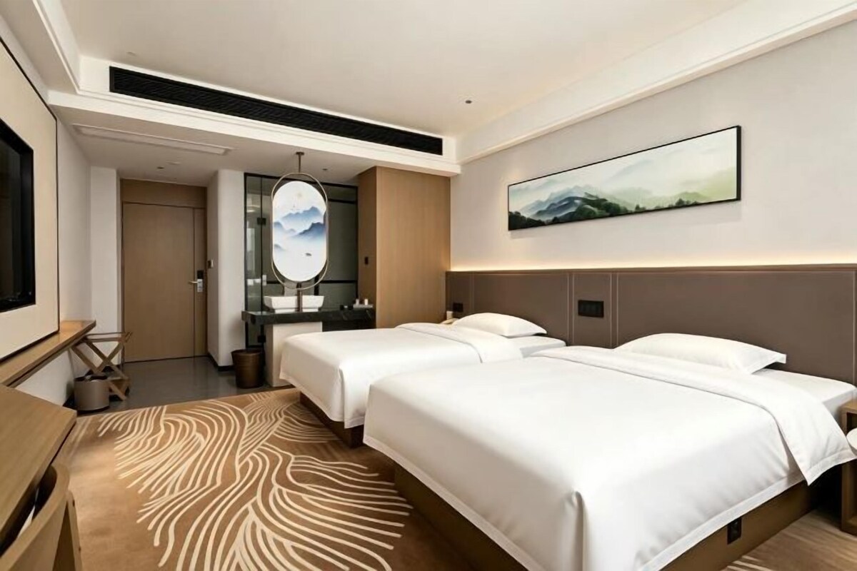 Une chambre d’hôtel avec deux lits, un grand miroir, un bureau et un tableau au mur.