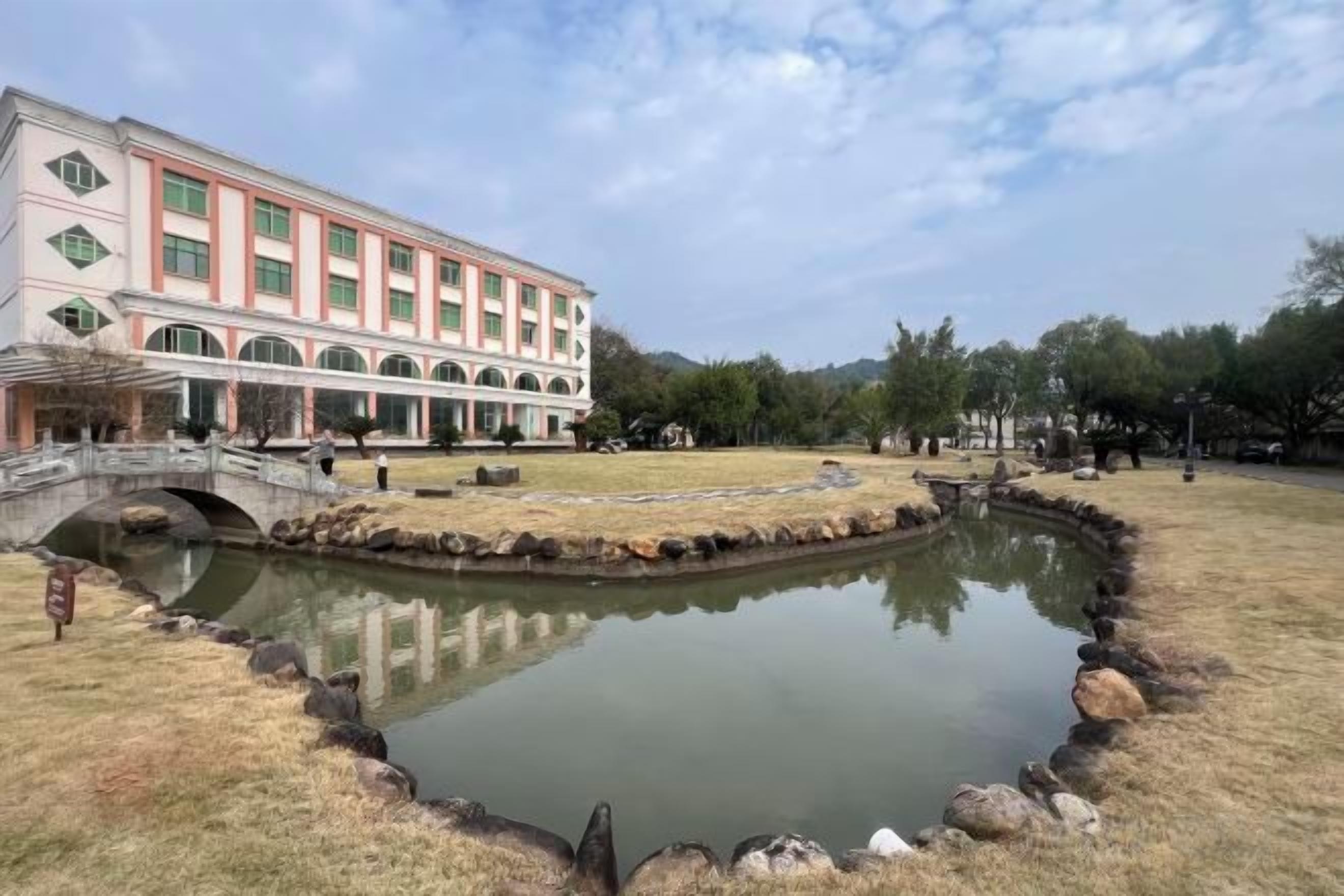 A building with a bridge, a pond, and a grassy area.