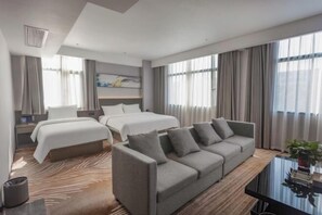 Ein Hotelzimmer mit Bett, Sofa, Schreibtisch und einem großen Fenster mit Vorhängen.