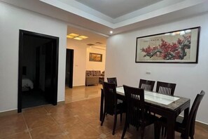 Un comedor con una mesa y sillas, una obra de arte enmarcada en la pared, y una puerta que da a otra habitación.
