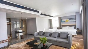 A modern hotel room with a sofa bed, a coffee table with a plant, a bathroom with a mirror, and a painting on the wall. - JAUNTYO INTERNATIONAL HOTEL (Dayu)