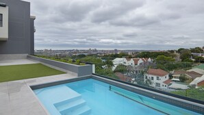 A rooftop pool with a city view, surrounded by greenery and residential buildings.