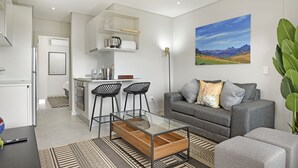 A modern living room with a glass coffee table, grey sofa, and a painting of a landscape.