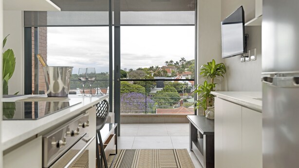 A modern kitchen with a large window, a flat-screen TV, and a view of the cityscape.