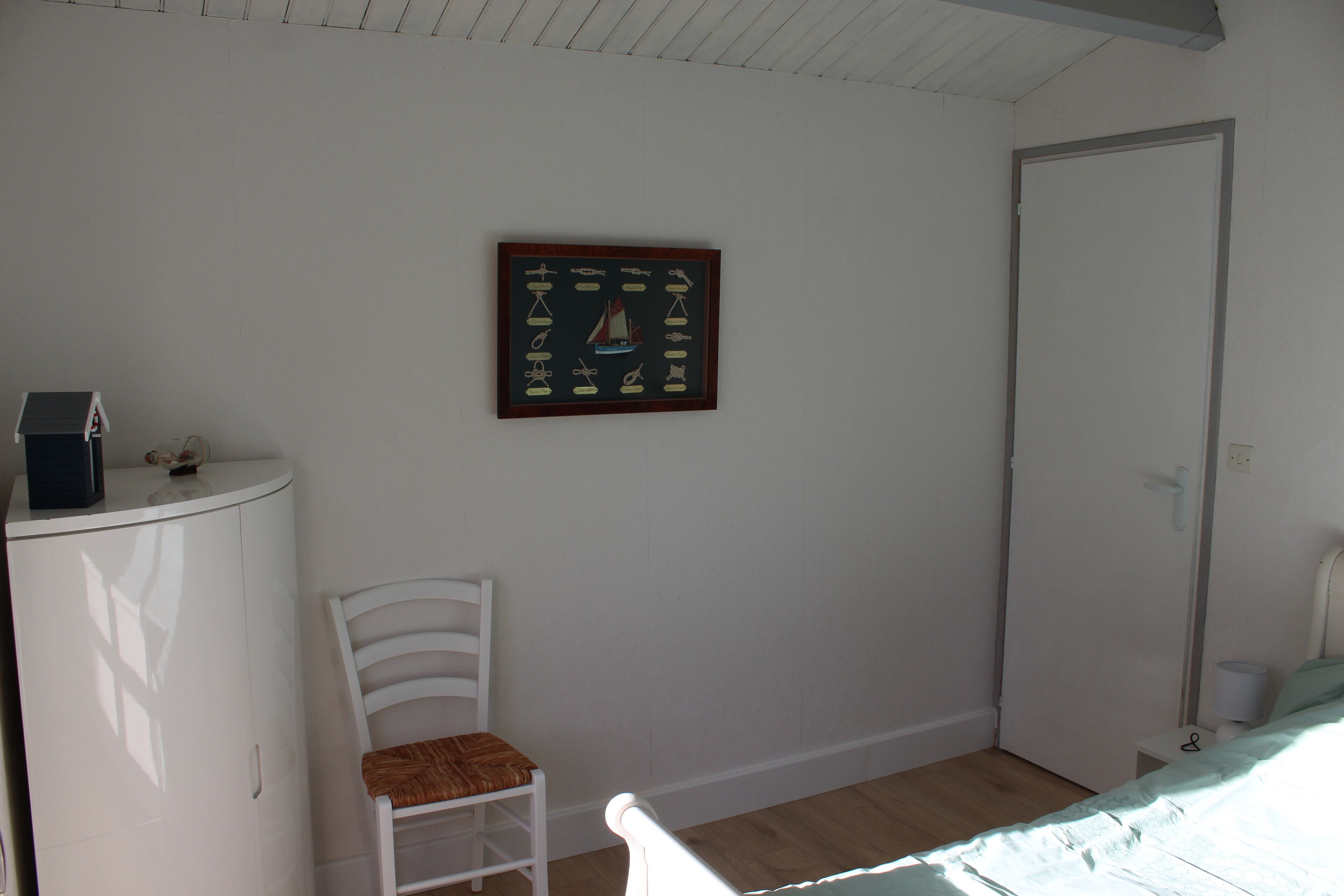 Un dormitorio con cama, una silla, un armario y un cuadro en la pared.