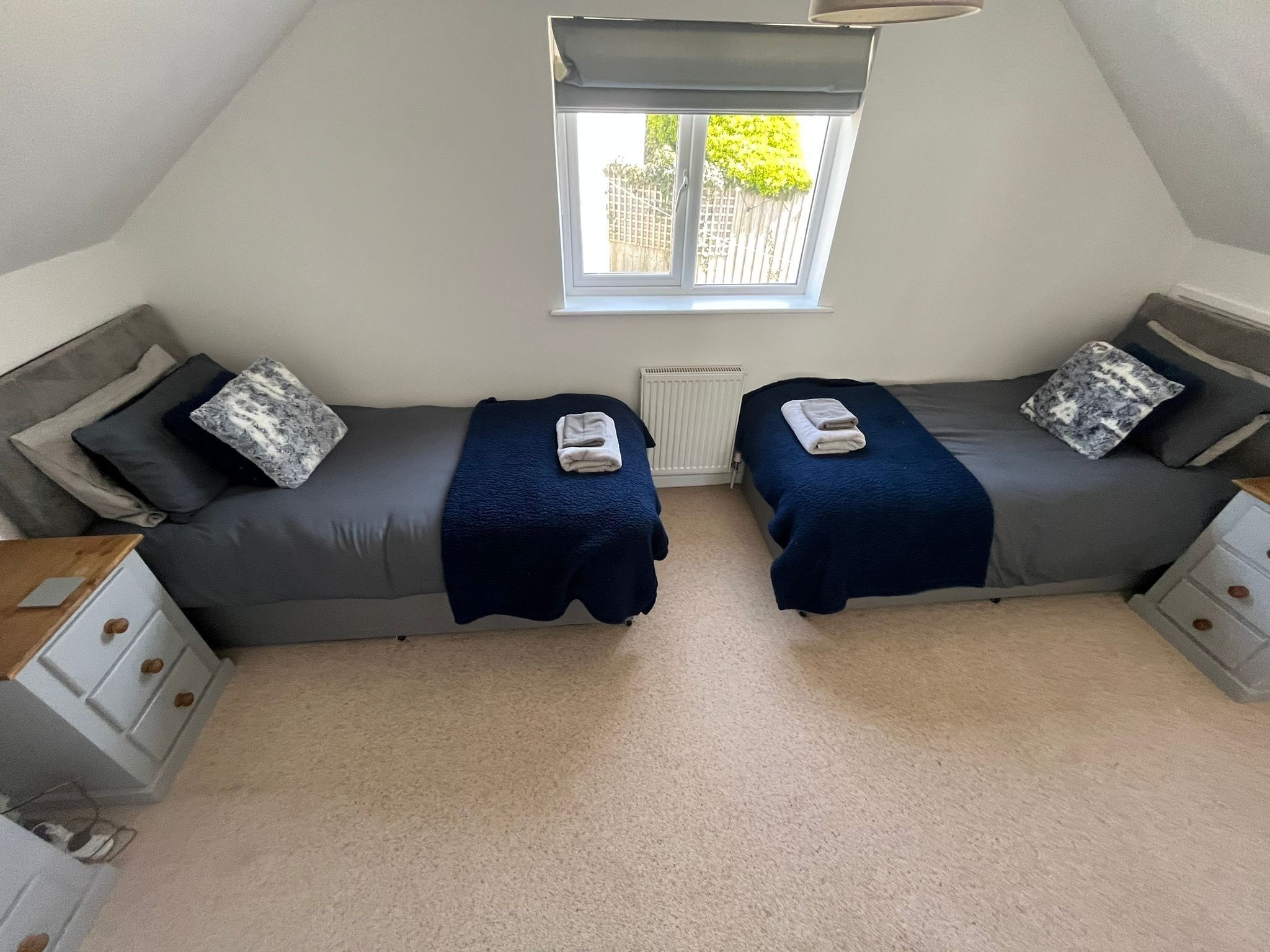 A small, cozy room with two beds, a window, and a radiator.