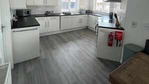 A modern kitchen with white cabinets, a black countertop, and a wooden table. - Bescot House, Bramble Hill, Bude, 4 bed det House (Bude)