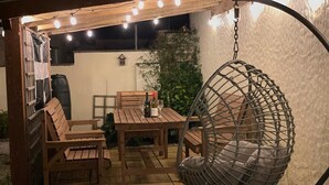 An outdoor patio with wooden furniture, a hanging chair, and string lights. - Bescot House, Bramble Hill, Bude, 4 bed det House (Bude)