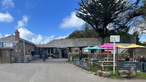 A stone building with a sign for 'The Lock Gates Cafe'. There are outdoor tables and umbrellas, and a sign asking if customers have paid and displayed. - Bescot House, Bramble Hill, Bude, 4 bed det House (Bude)