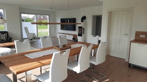 Una cucina moderna con un tavolo di legno e sedie bianche, un forno integrato e un televisore sopra il bancone.