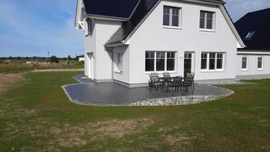 A two-story house with a patio area featuring a table and chairs. - New, exclusive vacation home close to the beach with sauna, 3 bedrooms, fireplace, WLAN, garage (Dranske-Lancken)