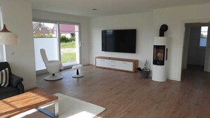 A modern living room with a flat-screen TV, a white sofa, a wooden coffee table, and a fireplace. - New, exclusive vacation home close to the beach with sauna, 3 bedrooms, fireplace, WLAN, garage (Dranske-Lancken)