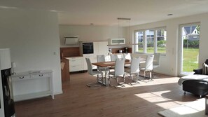 Una cucina moderna con mobili bianchi, un'area pranzo con tavolo in legno e sedie bianche, e ampie finestre che offrono vista sull'esterno.
