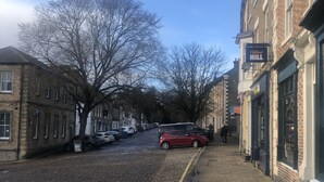 A cobblestone street lined with historic buildings, a red car parked on the side, and a sign for 'Mudlarks Spa 4 Paws' on the right. - Beautiful 2 bed Cottage in the Centre of Richmond (Richmond)
