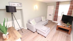 A living room with a grey sofa, a wooden coffee table, a floor lamp, and a television on a wooden stand. - Beautiful 2 bed Cottage in the Centre of Richmond (Richmond)