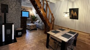 A cozy living room with a stone fireplace, a wooden staircase, a television, and a dining area with a table and chairs. - Chalet du Fayard in Belfahy, private Jacuzzi and view of the Vosges mountains (Belfahy)