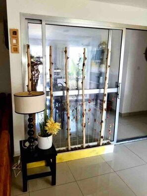 Une pièce dotée d’une porte-fenêtre coulissante, d’une petite table avec une lampe et un pot de fleurs, ainsi que d’une clôture décorative en bambou.